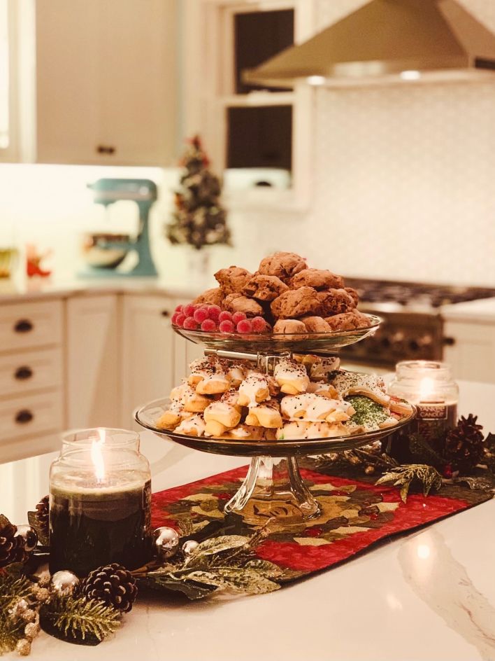 Beautiful double tier dish of homemade Christmas cookies with candles burning on either side in a farmhouse kitchen.